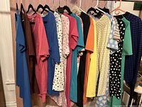 Photo of a rack with a line-up of 18 women's LulaRoe tops including t-shirts and one sweater in various colors and patterns showing variety and condition.
