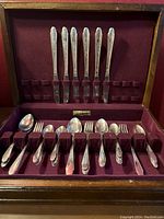 Wide shot of the open wooden flatware box showing various spoons, forks, and knives in maroon velvet slots.