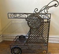 Side view of ornate wrought iron serving cart showing scroll details and lattice shelves