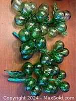 Three green glass grape clusters showing glossy translucent grapes with attached leaves and stems.