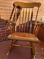 Full front view of the mid-century wooden rocking chair showing the spindle back and armrests with floral detailing on top board.