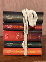Five paperback novels by Sarah J. Maas stacked with spines visible and bound with a beige fabric strap.