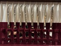 Silverplate knives with floral design handles in burgundy velvet slots inside cream lined wooden case.
