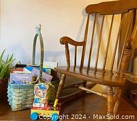 Wooden child's rocking chair with basket and toy beside it, showing side view.