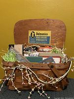Front view of vintage picnic basket filled with cookbooks and decorated with floral garland and faux grass