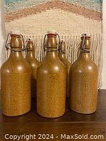 Front view of six beige stoneware beer bottles with ceramic stopper caps and metal wire closures.