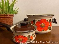 Photo shows two vintage enameled pots with bright orange poppy floral patterns. A larger 3-quart pot with two handles and a smaller sauce pot with a long handle and glass lid.