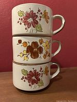 Side view of three stacked vintage Stonecrest mugs featuring brown, yellow, orange, green and red floral plum blossom patterns.