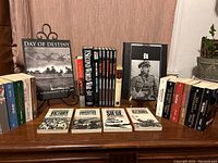 Full lot displaying 27 WWII history related books including paperbacks and coffee table books arranged on a wooden surface against a curtain background.