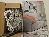 Opened box showing white cable and snowflake string lights next to the retail box of the moon lamp with living room design on packaging.
