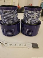 Two purple Dyson V10 motor filter replacements side by side with cleaning brush in front on a flat surface.