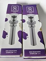 Two boxed sink drains with the M. Rosenfeld Home brand visible, labeled 'Sink Drain with Overflow 1 1/4'. Boxes show minor wear.