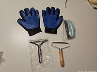 Two blue pet grooming gloves with rubber bristles and three pet hair lint removers of differing designs placed on a white surface.