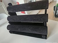 Three-tier black velvet jewelry bracelet holder stand laid on side showing three horizontal rods for bracelets or necklaces.