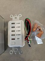 Close-up of a digital timer showing labeled push buttons for 2, 4, 8, 12 hours and OFF with attached wires and mounting hardware in plastic bag.