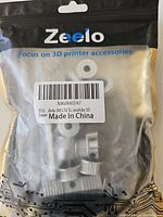 Packaged 3D printer accessory kit showing five stainless steel extrusion wheels and other small parts inside a clear plastic bag branded 'Zeelo'.