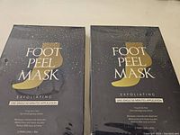 Two unopened black boxes of Aliceva Foot Peel Mask, labeled exfoliating, showing packaging and basic product details.