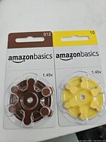 Photo showing two circular cards of AmazonBasics hearing aid batteries with tabs, one yellow (size 10) and one brown (size 312).