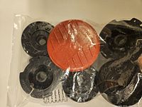 Two sealed plastic bags each containing six black plastic feedspools, one orange/red cap and one metal spring per bag for Black & Decker lawn mower models.