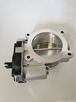 Side view of silver metal electronic throttle body with circular opening and black attached electronic control module