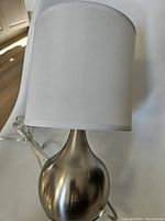 Table lamp showing the tear drop shape brushed nickel base with attached white fabric shade.