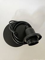 Black pendant light fitting with ceiling rose and E26/E27 lamp holder seen from side angle, cable coiled inside the base.