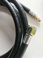 Close-up of brass and metal fittings on black flexible propane hose showing 3/8" flared nut and quick connect end.