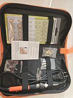 Opened kit with soldering and wood burning tool, power cord, multiple interchangeable tips held in plastic trays inside a black and orange carrying case along with instruction manual and accessory bags.