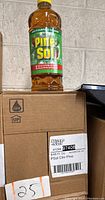 Photo showing one 48 fl oz bottle of Pine-Sol Original Multi-Surface Cleaner on top of a cardboard box labeled with product info indicating Pine-Sol cleaner in pine scent.