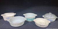 Full view of five vintage casserole dishes with various patterns in white milk glass and clear glass with lids