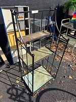 Full view of the metal plant stand showing three copper trays inserted and the black metal frame with decorative details.