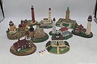 Overview of the ten Danbury Mint lighthouse figurines arranged on a white backdrop showing a variety of lighthouse styles and bases