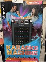 Front of the karaoke machine box showing brand, model, images of people singing, and colorful lights.
