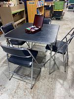 Black Samsonite card table with chrome legs and four matching folding chairs arranged around it, poker chip card box opened on table
