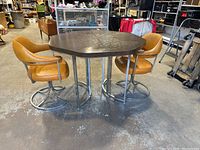 Photo of the Mid-Century Modern octagonal table with decorative embossed pattern and two brown vinyl swivel chairs with chrome bases.