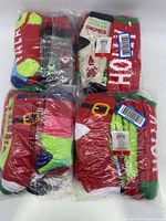 Four sealed plastic packs of holiday-themed socks featuring various Christmas designs and colors.