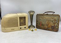 Overall lot view showing the radio, lunch box, pewter vase, and three buttons/pins.