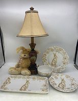 Full view of lamp, plush bunny toy, and set of bunny-themed dishes including large plate, small plate, platter and bowl.