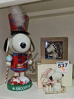 Photo showing full view of Snoopy nutcracker, Lenox sled ornament, and boxed Jim Shore Snoopy ornament.