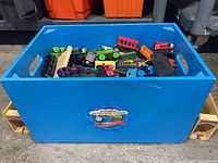 Blue plastic bin filled with assorted wooden Thomas the Tank Engine train cars and track pieces.