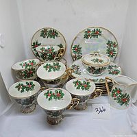 Full view of tea set showing 8 cups, various saucers, plates, creamer, and sugar bowl with lid, all decorated with a holly leaf and berry pattern with iridescence and gold trim.
