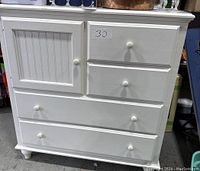 Front view of white wooden dresser showing three drawers and one cabinet door with knob handles.