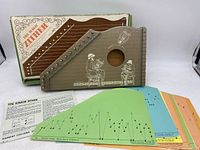 Junior Zither with original box and multiple colored music cards laid out in front.