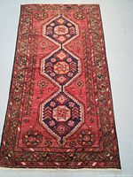 Full view of wool Persian rug showing rich rust-red field with navy blue medallions and tribal pattern