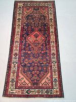 Full view of the navy blue background Persian rug with intricate medallion and floral designs bordered by cream and red edges.