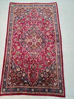 Full view of the rectangular Persian rug showing the red central field with intricate floral medallion and border patterns in blue, cream, and navy tones.