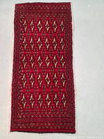 Full view of the rug laid flat on a gray floor showing entire patterned surface in deep red with geometric ornamentation.