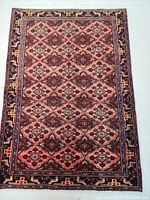 Full view of the Persian wool rug, displaying the all-over geometric panel pattern with reds, pinks, burgundy, black and beige colors.