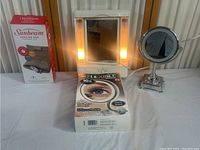 All items in lot displayed including Sunbeam heating pad box, lighted wall-mounted bathroom mirror, and My Flexible 10x magnifying makeup mirror.