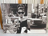 Frontal view of the Breakfast at Tiffany's poster showing Audrey Hepburn in signature look with ornate chandeliers in foreground.
